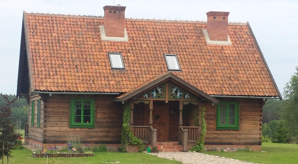 Domy z bali – parterowy dom drewniany z gankiem, zielonymi ramami okien i ceglanym dachem